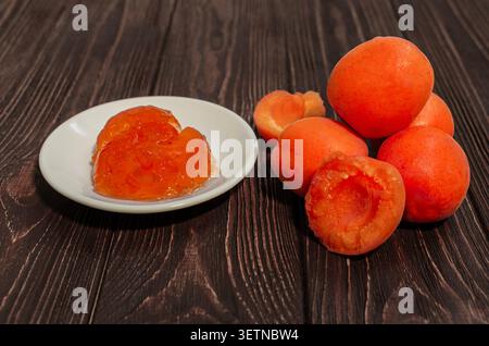 Aprikosenmarmelade in einer weißen Untertasse und frische reife Aprikosen auf dunklem Holzhintergrund. Stockfoto