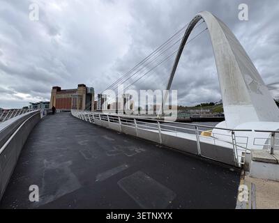Blick auf die Fußgängerbrücke Gateshead Millennium Bridge, die den Fluss Tyne zwischen Newcastle und Gateshead unter bewölktem Himmel überspannt. Stockfoto