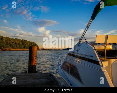 Ein kleines Motorboot liegt bei Sonnenuntergang an einem Pier am Hudson River bei Dobbs Ferry mit Blick auf das entfernte Manhattan Stockfoto