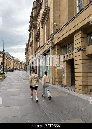 Ein junges Paar spaziert auf dem Bürgersteig an der Grey Street in Newcastle upon Tyne und zeigt die neoklassizistische Sandsteinarchitektur der Gegend. Stockfoto