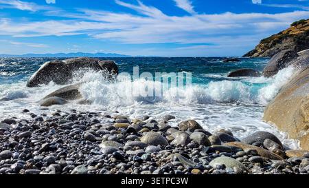 An einem Kiesstrand der Insel Elba in der Toskana, Italien, prallen Meereswellen gegen große Felsen. Stockfoto