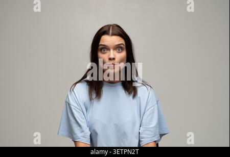 Junge Frau kreiert lustiges Fischgesicht, knisternde Lippen und sich weiternde Augen und vermittelt Überraschung und Humor mit spielerischem Ausdruck Stockfoto