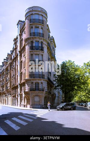 Ein klassisches Pariser Eckgebäude im Haussmann-Stil mit verzierten Steinfassaden und schmiedeeisernen Balkonen unter einem klaren blauen Himmel. Stockfoto