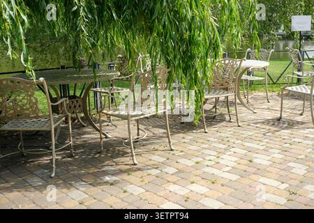 Ruhige Atmosphäre im Freien mit eleganten Metallstühlen und Tischen unter grünem Weidenlaub. Kiew, Ukraine, 23. Juni 2026 Stockfoto