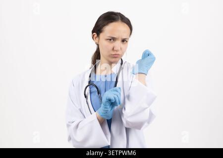 Eine junge Ärztin, die eine Spritze hält und sie auf weißem Hintergrund genau anschaut Stockfoto