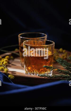 Whisky- oder Brandygläser auf Holztablett mit Mimosenblüten, elegante Getränke-Stilllife Stockfoto