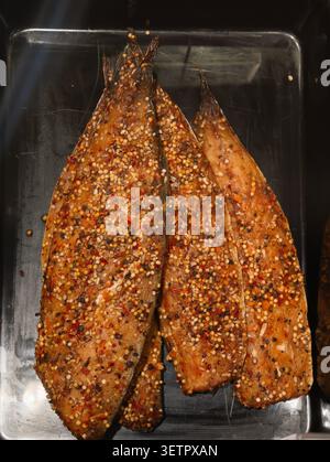 Nahaufnahme von drei gegrillten Fischfilets, die mit gepresstem rotem Pfeffer, ganzen Senfsamen, schwarzem Pfeffer und getrockneten Kräutern auf Hochglanz gewürzt sind Stockfoto