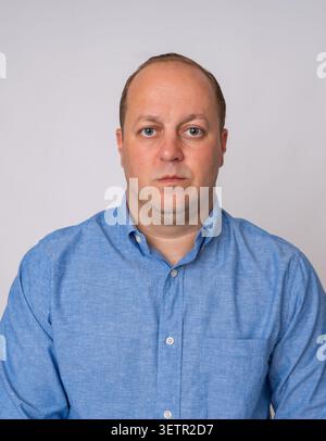 Studio-Kopfaufnahme eines selbstbewussten und ruhigen mittelgroßen Mannes, der ein lässiges blaues Button-Down-Hemd trägt und direkt in die Kamera blickt Stockfoto