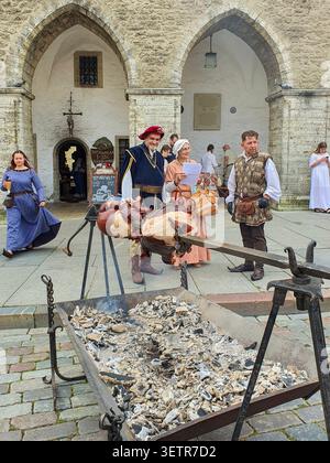 Tallinn, Estland - 15. August 2020: Ein Mann in mittelalterlicher Tracht brät Fleisch auf einer Spucke über heißen Kohlen unter den gotischen Bögen des Rathauses von Tallinn durin Stockfoto