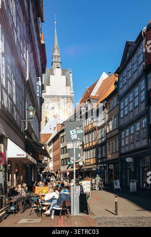 Hannover, Deutschland - 21. April 2026: Freiluft-Cafés und historische Fachwerkhäuser entlang einer engen Straße in der Altstadt von Hannover mit dem Turm Stockfoto