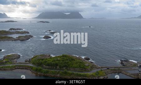 Atemberaubende Aussicht auf die Lofoten-Inseln mit dramatischen Gipfeln über das ruhige Meer, verstreute felsige Inseln, üppige grüne Vegetation und Stockfoto