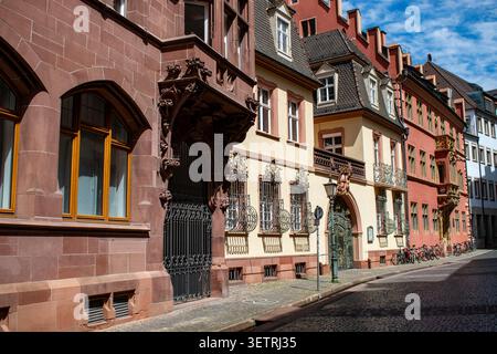Historische Sandstein- und pastellfarbene Gebäude mit kunstvollen schmiedeeisernen Balkonen säumen eine Kopfsteinpflasterstraße in der Altstadt von Freiburg im Breisgau Stockfoto