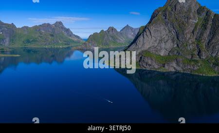 Atemberaubende Aussicht auf die Lofoten-Inseln mit steilen Granitgipfeln, tiefblauem Fjordwasser und üppigen grünen Hängen unter klarem Himmel mit Stockfoto
