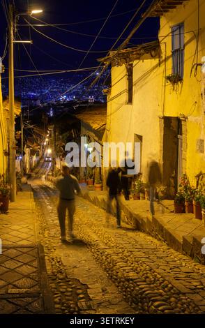 Touristen, die in der späten Nacht auf einer steilen, engen gepflasterten Straße in Cusco, Peru, spazieren gehen. Stockfoto