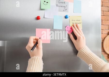 Person, die auf Haftnotizen an einer Kühlschranktür schreibt Stockfoto