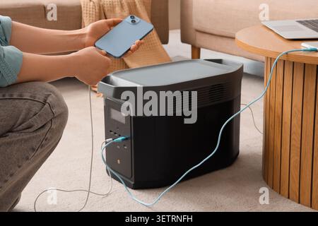 Person, die Smartphone und Laptop mit tragbarem Kraftwerk zu Hause auflädt Stockfoto