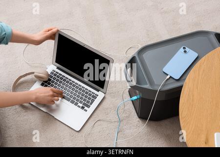 Person, die einen Laptop verwendet, der mit einem tragbaren Kraftwerk verbunden ist und das Smartphone auflädt Stockfoto