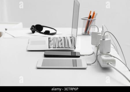Moderner Arbeitsbereich mit Laptop, Smartphone, Tablet und Ladeadapter auf weißem Schreibtisch Stockfoto