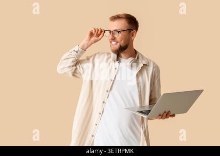 Ein lächelnder junger Mann hält einen Laptop und passt die Brille an Stockfoto