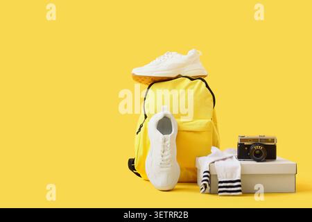 Weiße Turnschuhe mit gelbem Rucksack und Vintage-Kamera auf gelbem Hintergrund Stockfoto