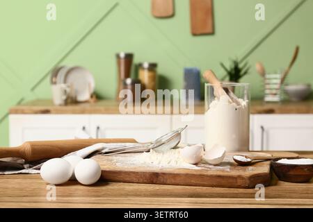 Schneidebrett mit Mehl, Eiern, Backpulver und Küchenutensilien zur Zubereitung von Teig auf Holztisch in der Küche Stockfoto