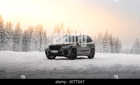 BMW X5 SUV fährt auf einer schneebedeckten Straße im Winter, umgeben von einem schneebedeckten Wald. Automobilfotografie mit einer dynamischen Außenszene. Stockfoto