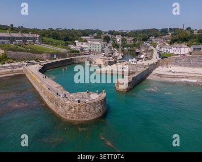 Niedrige Luftperspektive auf den historischen gekrümmten Steinpier und das türkisfarbene Wasser im Hafen von Charlestown, die Gebäude und Boote am Wasser vor Anker zeigt Stockfoto