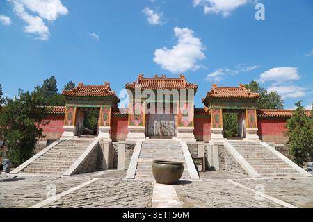 Ein großes dreifaches Tor zu den östlichen Qing-Gräbern, das traditionelle chinesische kaiserliche Architektur mit leuchtenden roten Wänden und kunstvollen goldenen Dekorationen zeigt Stockfoto