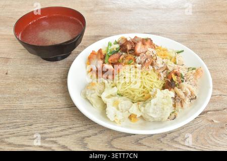 Trockene chinesische Ei gelbe Nudeln mit rotem Barbecue-Schweinefleisch und Knödel mit Krabbenfleisch auf Teller mit klarer Suppentasse Stockfoto