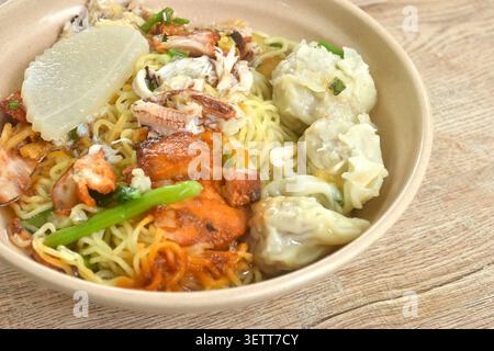 Chinesische Eigelnudeln mit rotem Barbecue-Schweinefleisch und Knödeln mit Krabbenfleisch in klarer Suppe auf einer Schüssel Stockfoto