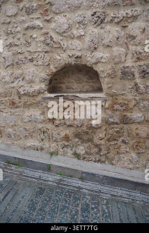 Alte Steinmauer mit einem kleinen Fenster in einer Stadtstraße Stockfoto