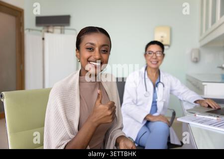 Glückliche junge afroamerikanische Patientin zeigt Daumen vor der Kamera Stockfoto