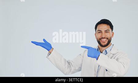 Arzt, Porträt oder Mann, der im Studio für Werbung oder Präsentation auf weißem Hintergrund zeigt. Männliche Person, medizinisches Fachpersonal oder Lächeln mit der Hand oder Stockfoto