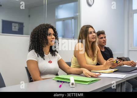 Junge Studenten, die an Schreibtischen sitzen, aufmerksam zuhören und an einer akademischen Vorlesung oder einem Seminar in einer zeitgenössischen Universitätsklasse teilnehmen Stockfoto
