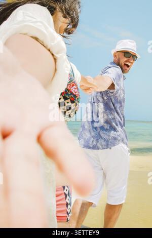 Fröhlicher junger Mann, der eine Frau führt, die Hände hält, zum Strand laufen, Spaß haben zusammen auf der flachen türkisfarbenen Meer Wasser Sandstrand tropische Insel reso Stockfoto