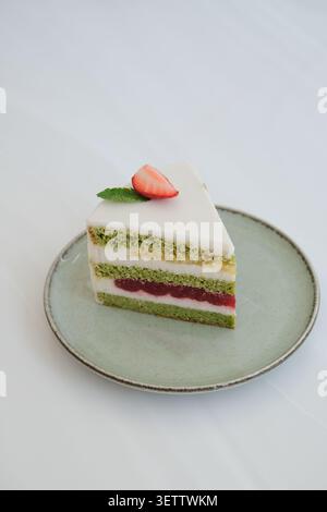 Mehrschichtige Dessertkuchenscheibe mit Erdbeergarnitur auf Keramikplatte vor sauberem weißem Hintergrund Stockfoto