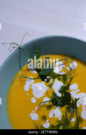 Elegante Orangen-Gemüsesuppe in blauer Schüssel mit Creme und frischen Erbsensprossen Stockfoto