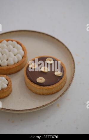 Elegante Desserttörtchen mit Schokoladenglasur und Sahnefüllung auf Keramikplatte Stockfoto