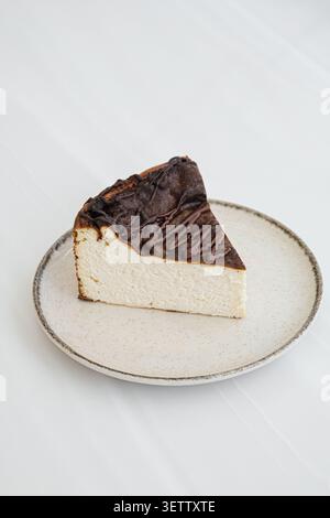 Gebrannte Käsekuchenscheibe mit Schokoladenbesatz auf gesprenkelter Keramikplatte gegen sauberes weiß Stockfoto