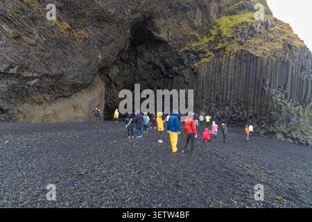 Touristen stehen neben der massiven Basaltsäulenhöhle Hálsanefshellir am schwarzen Sandstrand von Reynisfjara in Island. Stockfoto