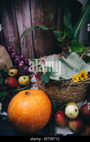 Ein rustikales Stillleben im Herbst mit einem großen orangen Kürbis, frischen roten und grünen Äpfeln, Trauben und einem Korb mit hellgrünem Leinen, dez Stockfoto