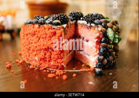 Eine Nahaufnahme eines appetitlichen rosafarbenen Kuchens mit einer geschnittenen Scheibe, bedeckt mit einer strukturierten roten Krümelbeschichtung und einem großzügigen Sortiment Stockfoto