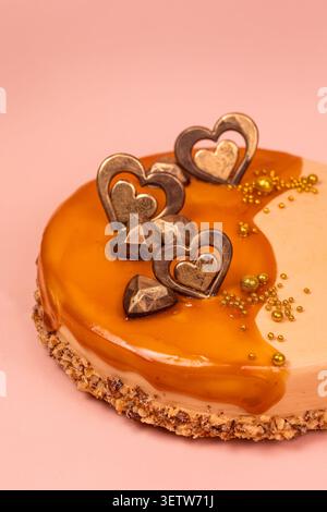 Eine mittelgroße Nahaufnahme eines handwerklich hergestellten Karamelltortes mit makellos glänzenden Glasur-Tropfen, strukturierter Nusskruste und detaillierten Schokoladenherzen von Stockfoto