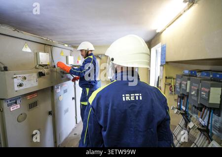 Zwei Techniker, die Schutzhelme und Sicherheitsausrüstung tragen, bedienen schwere Maschinen in einer elektrischen Unterstation. Stockfoto
