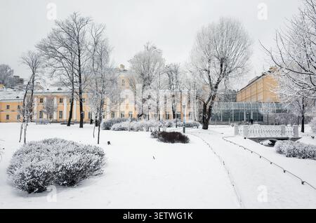 Ein landschaftlich schöner, schneebedeckter Park mit satinierten Bäumen und historischen gelben Gebäuden, die eine ruhige und magische Winteratmosphäre in einer urbanen Umgebung hervorrufen Stockfoto