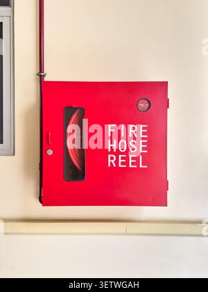 Roter Metallschlauchschrank, montiert an der Gebäudewand, Nahaufnahme des gewerblichen Brandschutzsystems mit Kopierraum Stockfoto