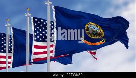 Die Flaggen des Bundesstaates Idaho schwenken zusammen mit den Nationalflaggen der Vereinigten Staaten von Amerika an einem klaren Tag. 3D-Illustrationen rendern. Geriffeltes Material. Selektiver Fokus - Fotomontage Stockfoto