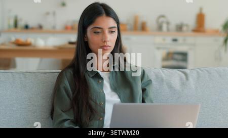 Konzentrierte arabische indische Frau, die auf Laptop zu Hause Couch fokussierte freiberufliche Studentin weibliche hispanische Dame, die im Internet surft Fernarbeit Stockfoto