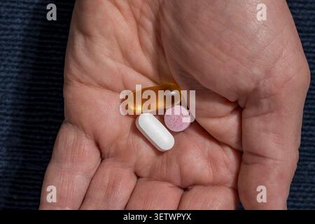 Nahaufnahme einer Hand mit verschiedenen Pillen und Vitaminkapseln. Ansicht von oben auf menschliche Palme, die medizinische Pillen und Omega-Kapseln auf dunklem Hintergrund hält Stockfoto