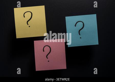 Gelb rosa und blaue Papiere mit handgeschriebenen Fragezeichen auf einer dunklen Oberfläche. Minimalistisches Konzept für Kundensupport-FAQ-Seiten, Auswahl, Gehirn Stockfoto